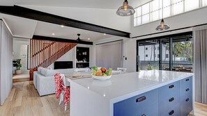 A modern kitchen with a central island, a dining area with a sofa, and a staircase leading to an upper level. - Harper - the perfect holiday home (3 Bedroom) (Mission Beach)