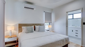 A hotel room with a bed, bedside lamps, a wardrobe, and an air conditioning unit. - Harper - the perfect holiday home (3 Bedroom) (Mission Beach)