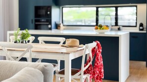 A modern kitchen with a central island, white chairs, and a dining table. - Harper - the perfect holiday home (3 Bedroom) (Mission Beach)