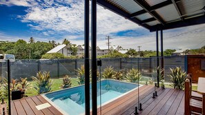 A swimming pool with a wooden deck, surrounded by a metal fence, under a clear sky. - Harper - the perfect holiday home (3 Bedroom) (Mission Beach)