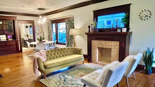 A living room with a sofa, armchair, and a fireplace. There is a dining area with a table and chairs in the background.