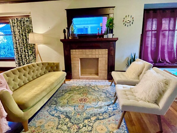 A living room with a beige sofa, a white armchair, a patterned rug, a fireplace, and a television. - Beautiful, family-friendly Portland home, walk score of 94! (Portland)