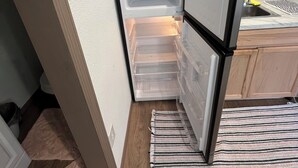 A compact kitchen with a refrigerator, microwave, and a small sink. - Shaanti Living • Cozy Studio Blue (Melrose)