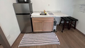 A compact kitchen with a refrigerator, microwave, sink, and a small dining area with a bench. - Shaanti Living • Cozy Studio Blue (Melrose)