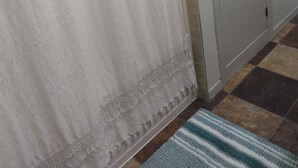 A bathroom with a white shower curtain, a white cabinet with two doors, and a patterned floor rug. - Cozy refreshed 2-bedroom bungalow with AC, WiFi in historic Pipestone, MN (Pipestone)