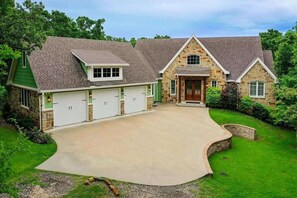 A two-story house with a garage, stone exterior, and a well-maintained lawn. - Coral Cove: Luxury Lake Retreat with Nature Views and Hot Tub (Oak Point)