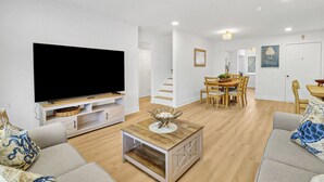 A living room with a flat-screen TV, a coffee table, and a dining area with a wooden table and chairs. - Coastal 4BR Oasis: Close to the Beach & Coligny Plaza (Hilton Head Island)