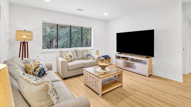 A living room with a sofa set, a coffee table, a TV on a stand, and a window with blinds. - Coastal 4BR Oasis: Close to the Beach & Coligny Plaza (Hilton Head Island)
