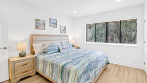 A bedroom with a bed, bedside tables, a wooden dresser, a window with blinds, and wall art. - Coastal 4BR Oasis: Close to the Beach & Coligny Plaza (Hilton Head Island)