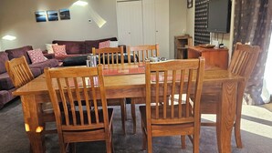 A living room with a wooden dining table, multiple wooden chairs, a sofa set, and a television mounted on the wall. - Rural, idyllic, and 360 degree views! Spacious and only 15 minutes from Wanaka. (Hāwea Flat)