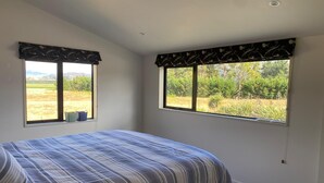 Un dormitorio con cama, dos ventanas con cortinas y vista a un campo.