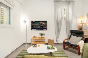 A living room with a flat-screen TV, a wooden side table, a black leather chair, and a green rug.