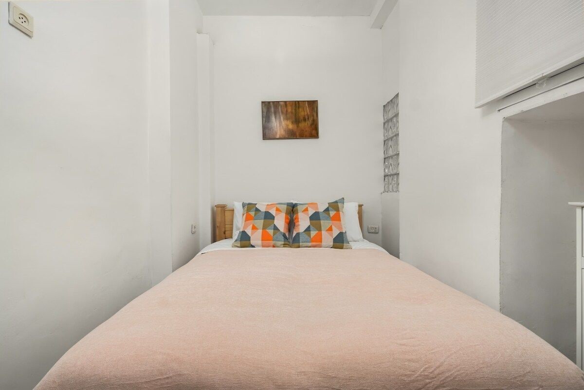 Een eenpersoonsbed met een roze sprei en twee kussens met een geometrisch patroon.