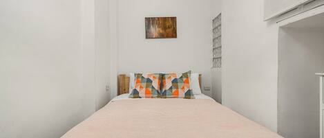 A single bed with a pink bedspread and two pillows with a geometric pattern.