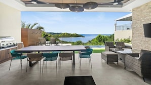 An outdoor patio with a dining table and chairs, a grill, and a view of the sea.