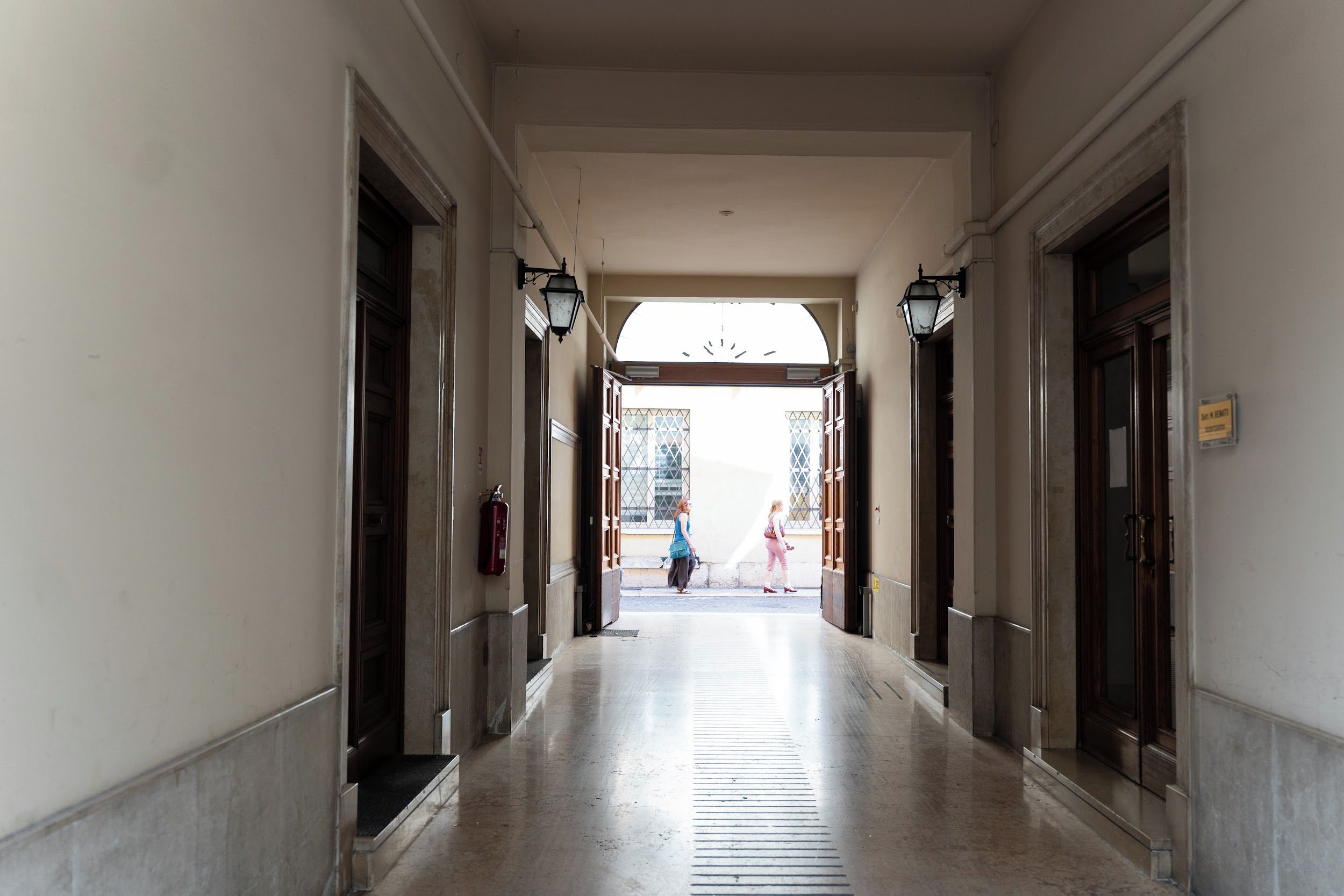 Un couloir avec des portes des deux côtés, un extincteur fixé au mur, et une vue dégagée sur la rue.