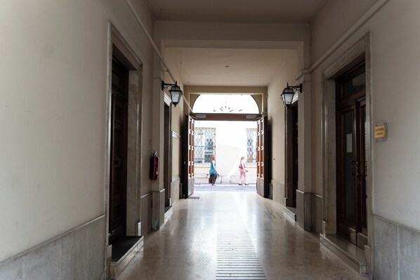 A corridor with doors on both sides, a fire extinguisher mounted on the wall, and a clear view of the street outside.
