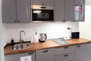 A modern kitchen with grey cabinets, a stainless steel sink, a kettle, and a coffee maker.