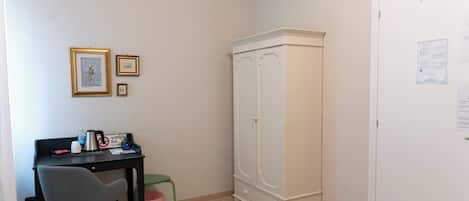 Et lille værelse med skrivebord, stol, garderobe og skraldespand.