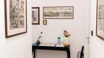 Un couloir avec une porte blanche, une console noire sur laquelle est posé un vase de fleurs, des tableaux encadrés et un magazine sur le sol.
