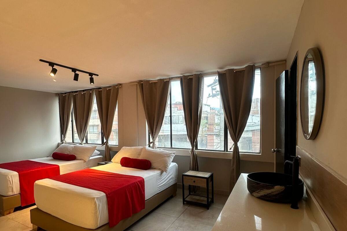 A hotel room with two beds, a small table, a TV, and a window with curtains.