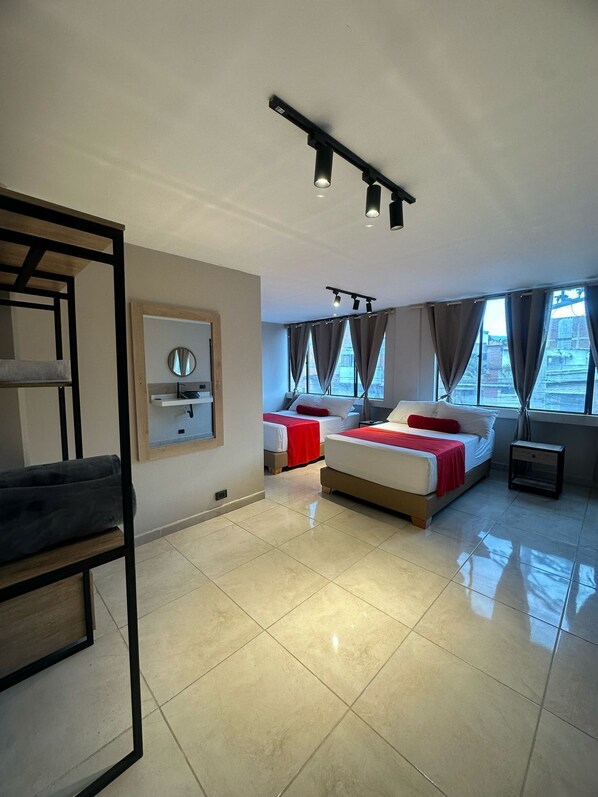A modern hotel room with a bunk bed, a single bed, a small desk, a mirror, and a large window with curtains. - Coral Boutique Hotel (Medellín)