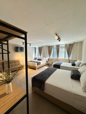 A modern hotel room with a large bed, two smaller beds, a sofa, a TV, and a window with curtains. - Coral Boutique Hotel (Medellín)