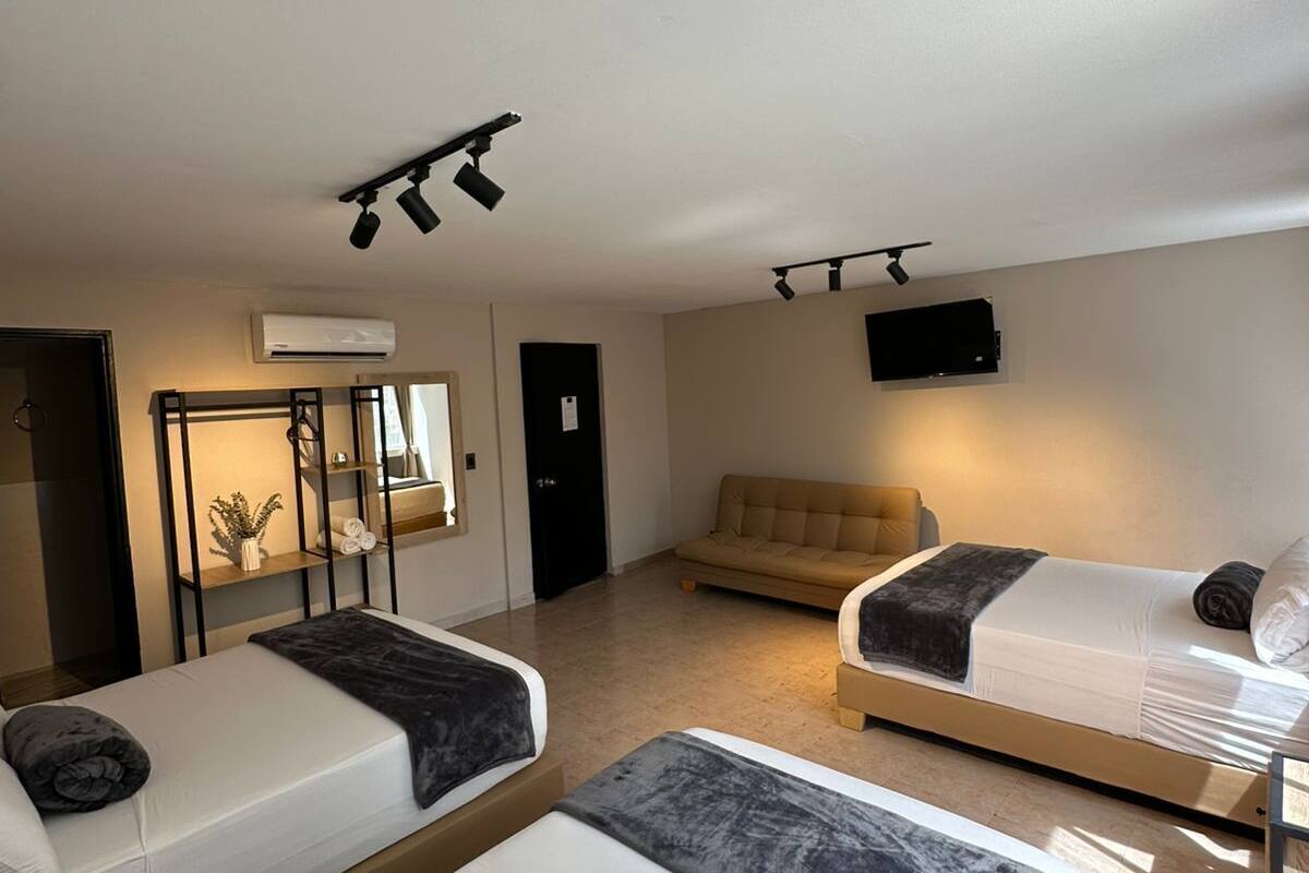 A hotel room with two beds, a sofa, a TV, and a mirror.