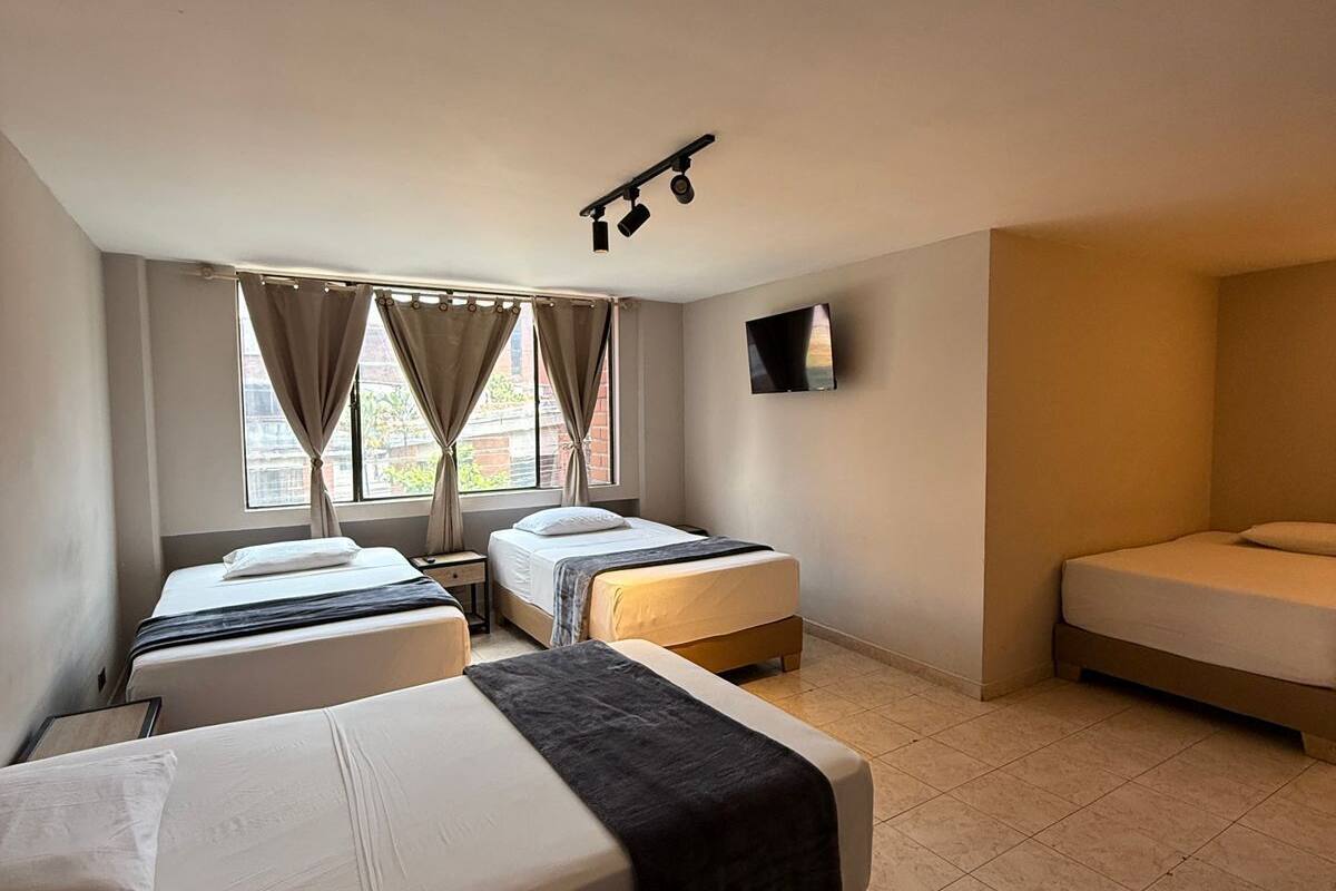 A hotel room with three beds, a flat-screen TV, and a ceiling light fixture.