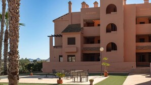 Un hotel de varios pisos con balcones, mobiliario exterior y una vista despejada de las montañas al fondo.
