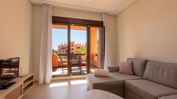 A modern living room with a sofa, a TV, and a balcony with a table and chairs.