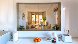 A modern kitchen with a large mirror, a dining area with a table and chairs, and a fruit bowl on the counter.