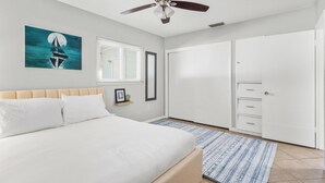 A bedroom with a bed, a ceiling fan, a painting of a sailboat, a window with blinds, and a wardrobe.