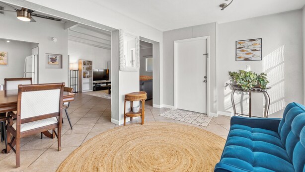 A modern living room with a blue sofa, a dining table with chairs, a woven rug, and a kitchen area in the background.
