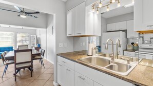 A modern kitchen with white cabinets, granite countertops, and stainless steel appliances. There is a dining area with a table and chairs visible in the background.