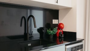 A modern kitchen with a black countertop, a black faucet, a red kettle, and a potted plant.