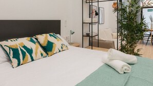 A neatly made bed with patterned pillows, a green towel, and a small bedside table with a lamp.