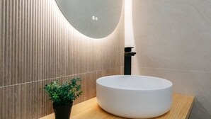 A modern bathroom with a round white sink, a black faucet, and a potted plant on a wooden countertop.
