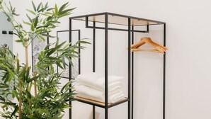 A minimalist room with a black metal shelving unit, a wooden hanger, and neatly folded white towels.