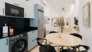 A modern kitchen with a microwave, oven, and washing machine. There is a dining area with a round table and chairs.