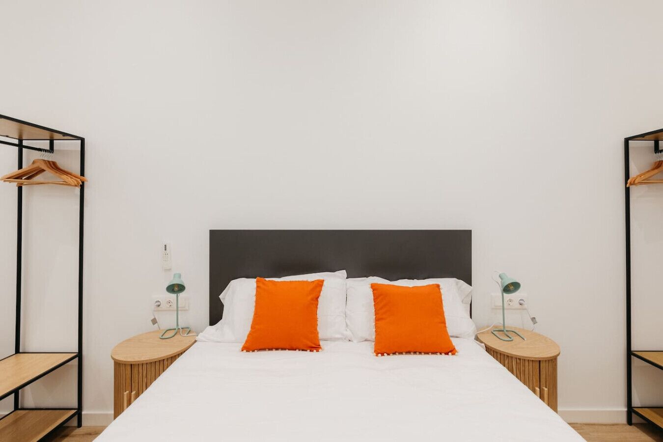 Una cama bien hecha con ropa de cama blanca y naranja, flanqueada por dos mesitas de noche con lámparas y estantes.