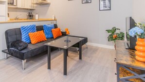 Uma sala de estar moderna com um sofá preto, almofadas coloridas, uma mesa de centro preta e uma mesinha de madeira com velas laranja.