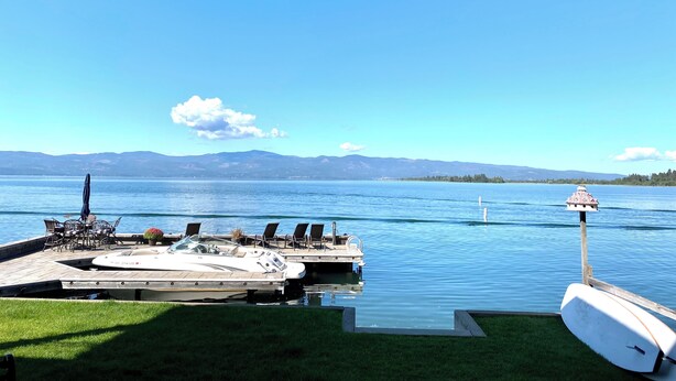 A dock with boats, a grassy area, and a clear view of a lake with mountains in the background. - THE FOX HOUSE on Flathead Lake: Lakefront Luxury Living (Bigfork)