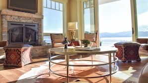 A spacious living room with a stone fireplace, comfortable seating, and large windows offering a view of the ocean. - THE FOX HOUSE on Flathead Lake: Lakefront Luxury Living (Bigfork)