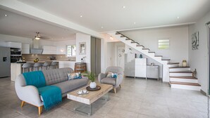 A spacious living area with a sofa, armchair, and coffee table. A kitchen is visible in the background, and a staircase leads to another level.