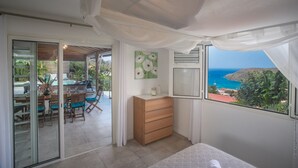 A bedroom with a bed, a dresser, and a view of the ocean.