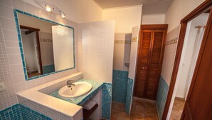 Ein Badezimmer mit einem weißen Waschbecken, blauen Fliesenwänden, einer Holztür und einem Spiegel über dem Waschbecken.