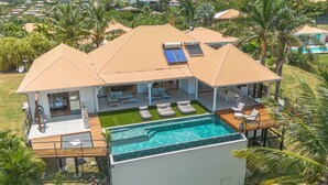 A modern house with a large swimming pool, multiple lounge areas, and a covered patio. - Luna Moona (Le Vauclin)
