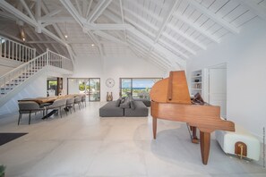 Relax in a spacious living area with a grand piano, dining space, and large windows offering a view of the outdoors.