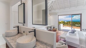 A modern bathroom with two large sinks, a large mirror, and a view of a bedroom with a bed and a balcony. - Luna Moona (Le Vauclin)